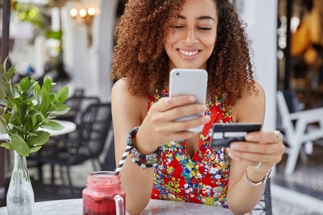cropped shot beautiful african american woman with happy look holds modern cell phone credit card makes shopping online